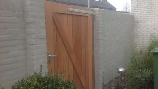 Plaatsen van een hardhouten pen-gat-poort in Goirle, de poort staat tussen twee tuinmuren