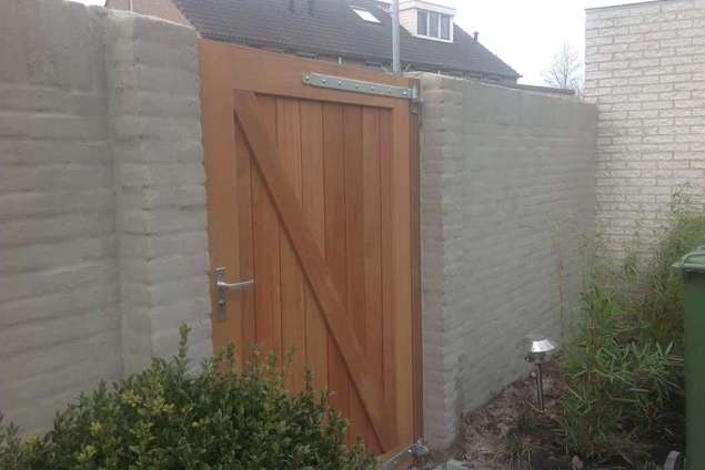 Plaatsen van een hardhouten pen-gat-poort in Goirle, de poort staat tussen twee tuinmuren